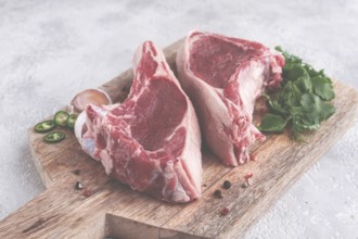 Fresh pieces of beef on the bone, on a wooden cutting board, with herbs and spices, ready for