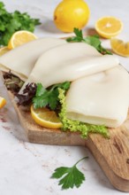 Fresh squid prepared for cooking, surrounded by herbs and lemon, placed on a wooden chopping board