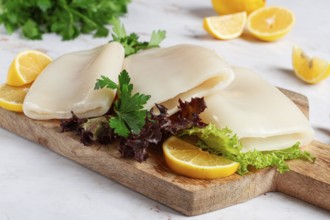 Fresh squid prepared for cooking, surrounded by herbs and lemon, placed on a wooden chopping board