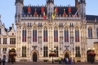 Tourist group looking at illuminated historic town hall of Bruges on Castle Square in the evening