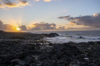 Dramatic cloudy sky with sunbeams at sunset, seaside coast with volcanic rocks, La Santa,