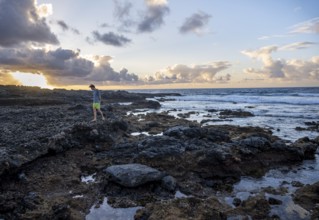 Tourist strolling on seaside coast with volcanic rocks at sunset, La Santa, Lanzarote, Canary