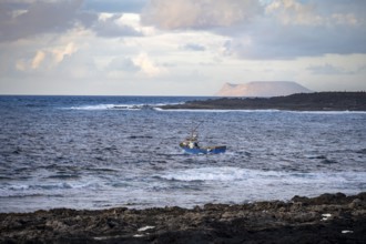 Fishing boat out to sea in the evening, seaside coast with volcanic rocks at sunset, La Santa,