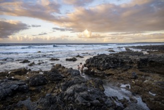 Tourists swim in the sea on rocky coast at sunset, La Santa, Lanzarote, Canary Islands, Spain
