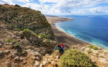 Female hiker climbing to Castillejo summit, view from the Risco de Famara cliffs of the coast and