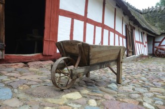 Old-fashioned wheelbarrow on paving stones and at half-timbered house in Den gamle by, The old
