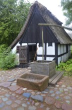 Older half-timbered house with thatched roof by older well in Den gamle by, The old village, open