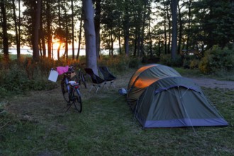 Tunnel tent, e-bike, cookware, two camping chairs on a campground at Lake Ringsjön, sunset, Horby,