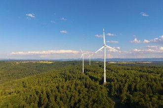 Green forests with several wind power plants under vivid blue sky with clouds, near Schorndorf,
