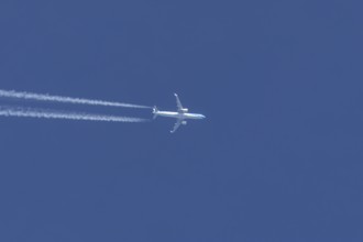 Jet passenger aircraft flying in a blue sky with contrails or vapour trails behind, England, United