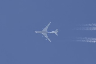 Boeing 747 jumbo jet cargo aircraft flying in a blue sky with contrails or vapour trails behind,
