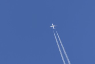 Jet passenger aircraft flying in a blue sky with contrails or vapour trails behind, England, United