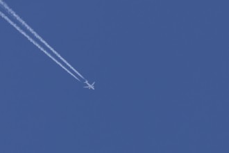 Airbus jet passenger aircraft flying in a blue sky with contrails or vapour trails behind, England,