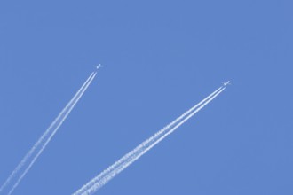 Two jet passenger aircraft flying in a blue sky with contrails or vapour trails behind, England,