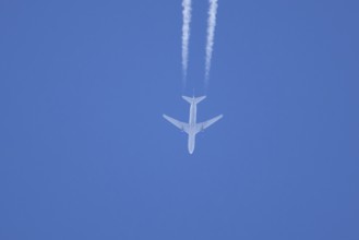 Jet passenger aircraft flying in a blue sky with contrails or vapour trails behind, England, United