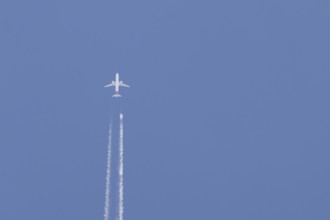 Airbus jet passenger aircraft flying in a blue sky with contrails or vapour trails behind, England,