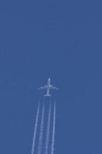 Jet commercial passenger aircraft flying in a blue sky with contrails or vapour trails behind,
