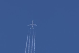 Jet commercial passenger aircraft flying in a blue sky with contrails or vapour trails behind,