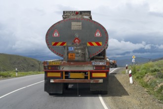 A truck drives on a winding road through a mountainous landscape under cloudy sky, truck with