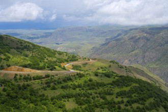 Wide green landscape with hills and a winding road under cloudy sky, landscape near Ltsen, Syunik