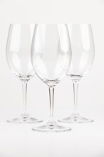 Three elegant, transparent wine glasses with long stems against a neutral background