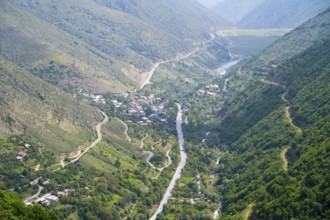 View of a village in the valley surrounded by green hills and a river, with winding roads through