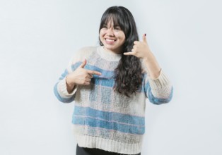 Cheerful asian woman gesturing CALL ME in sign language isolated. Beautiful girl making gesture