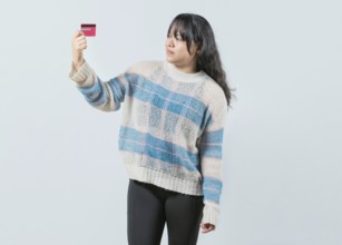 Confused asian girl holding a credit card isolated. Unsure and confused young woman holding and
