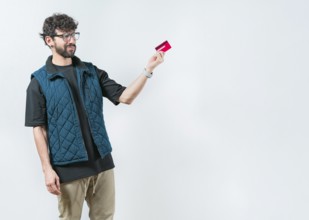 Unsure and confused young man holding and looking at a credit card. Confused modern guy holding a