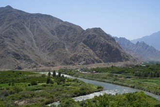 A river flows through a lush green landscape against a mountain backdrop, view of Iran, Aras River