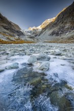 Ice structures on mountain stream with autumnal larches and mountain panorama, Ferpecle glacier,