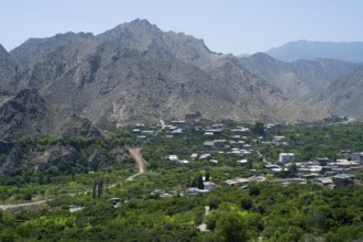 Mountain village with lush vegetation, surrounded by imposing mountains and clear blue sky, Meghri,