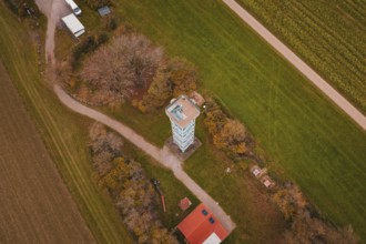 An observation tower in the middle of a rural landscape with fields and buildings, surrounded by