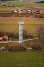 An observation tower in the middle of a rural landscape with fields and buildings, surrounded by