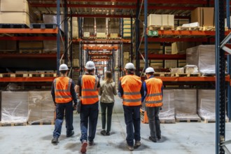 Warehouse manager and four workers wearing safety vests and hard hats walking through an industrial