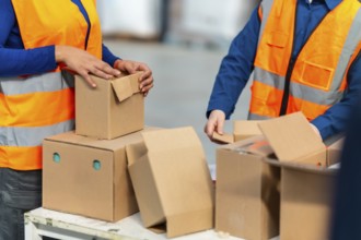 Warehouse workers in safety vests pack and sort cardboard boxes for shipment, demonstrating