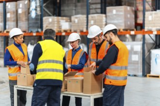 Diverse warehouse team in hardhats and hi vis vests sorting and packing cartons on a long table