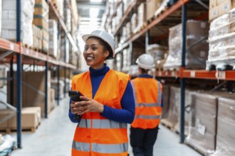Young woman worker smiling, wearing a safety vest and hardhat, holding a barcode scanner while