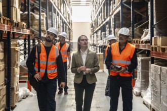 Diverse logistics team led by a female manager inspects inventory and scans boxes between tall