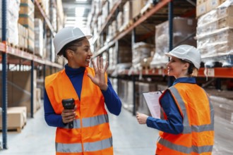 Two smiling female logistics workers wearing hard hats and safety vests collaborating while working
