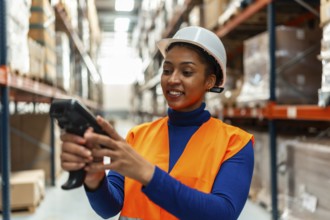 Young woman warehouse worker in safety hard hat and reflective vest scanning inventory with a