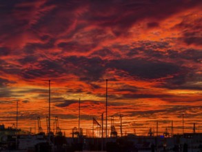 Dramatic sunset sky at Hamburg's Landungsbrücken with silhouetted cranes, ship masts and wind
