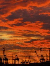 Dramatic sunset sky at Hamburg's Landungsbrücken with silhouetted cranes and wind turbines in the