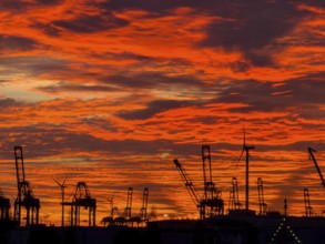 Dramatic sunset sky at Hamburg's Landungsbrücken with silhouetted cranes and wind turbines in the