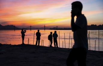 People enjoy the vibrant sunset by the Brahmaputra riverside, capturing photos and moments against