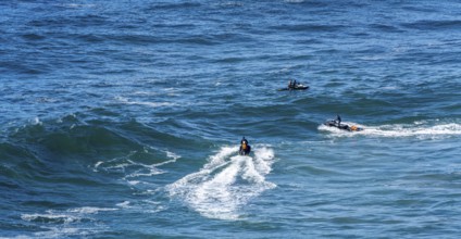 Surfers with their jet ski pilots in the Atlantic waves below Farol de Nazaré, Forte São Miguel,