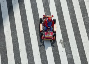 People in costumes drive small go-kart racing cars across zebra crossings, Shibuya Crossing,