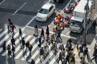 People cross zebra crossings, people in costumes ride small go-kart racing cars, Shibuya Crossing,
