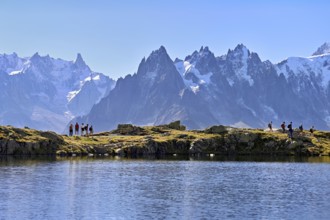 A group of hikers at Lac de Chésserys, behind the snow-covered Mont Blanc massif,