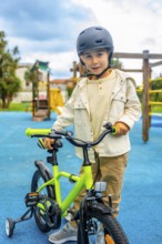 Young boy wearing a helmet standing and holding the handlebars of his bicycle with training wheels